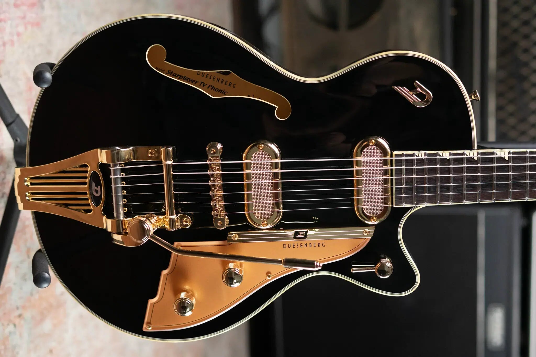 Black and gold electric guitar on a stand with a blurred background