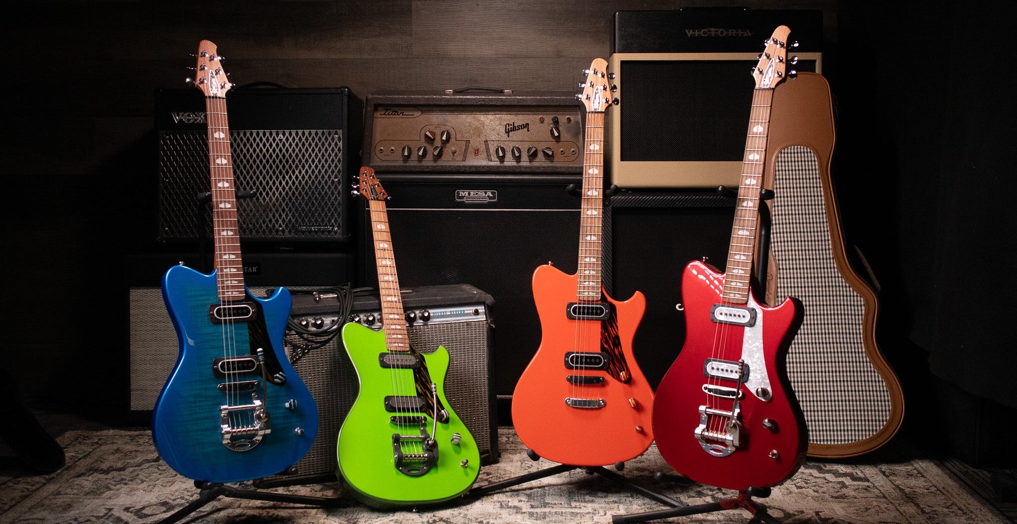 Four colorful electric guitars on stands with amplifiers in the background.