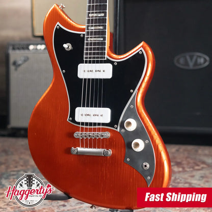Electric guitar with a red finish and black pickguard, branded 'Haggerty's', in front of an amplifier.